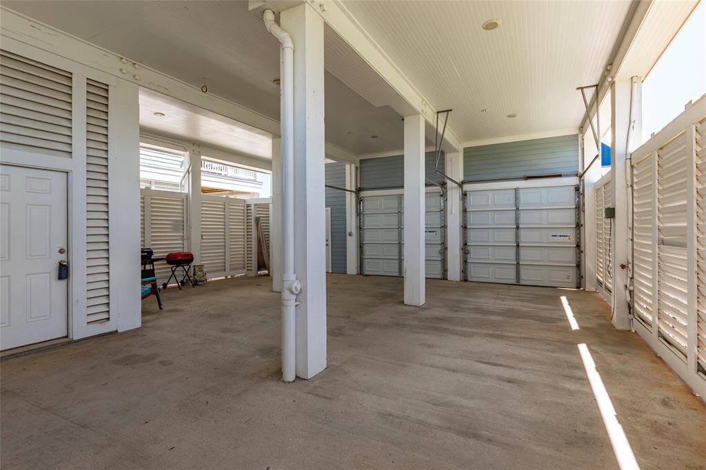 Spacious covered parking area with multiple garage doors, offering ample storage and vehicle space. Features a light, airy atmosphere with high ceilings and white paneling.