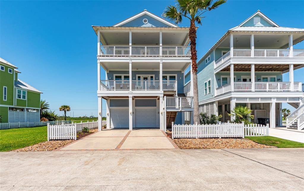 This coastal home features three stories with expansive balconies, ideal for enjoying ocean views. It has a modern design, a double garage, and charming white picket fencing.