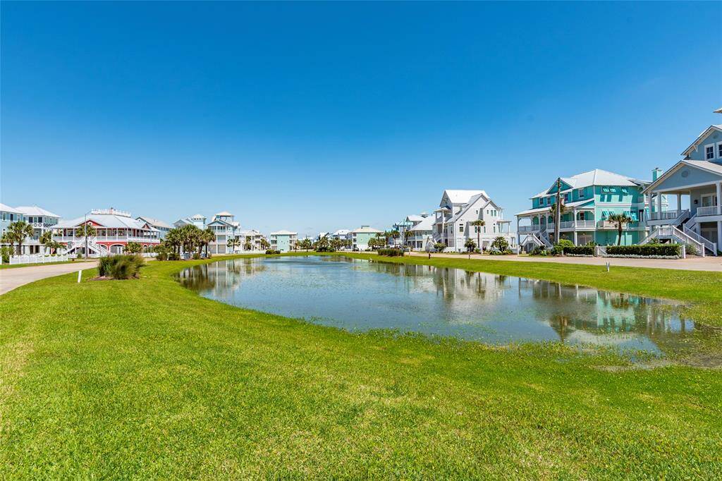 This photo showcases a serene neighborhood with charming coastal homes lining a calm waterway. The area features lush green lawns and a clear blue sky, offering a picturesque, tranquil setting ideal for relaxation and outdoor enjoyment.