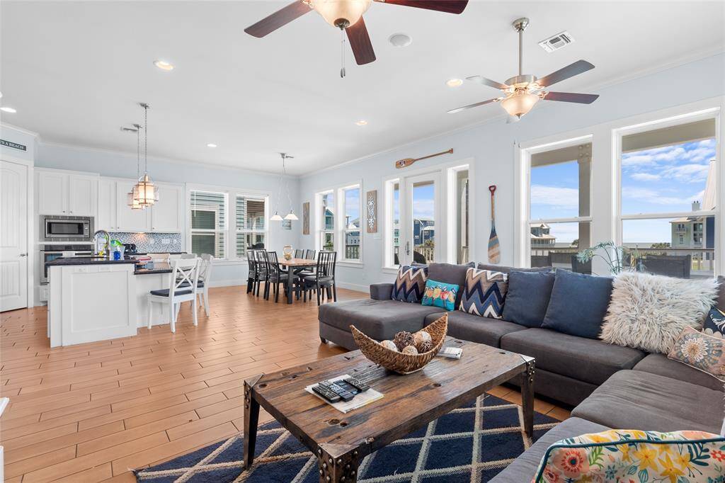 Spacious, open-concept living area with abundant natural light, featuring a modern kitchen with white cabinetry, a cozy dining area, and a comfortable living room with a sectional sofa. Large windows offer scenic views, and ceiling fans enhance comfort. Perfect for entertaining and relaxation.