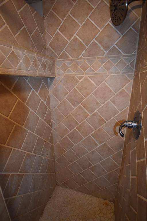 This photo shows a shower with beige diagonal tile walls, a built-in shelf, a modern showerhead, and a pebble-style floor, offering a cozy and stylish bathing space.