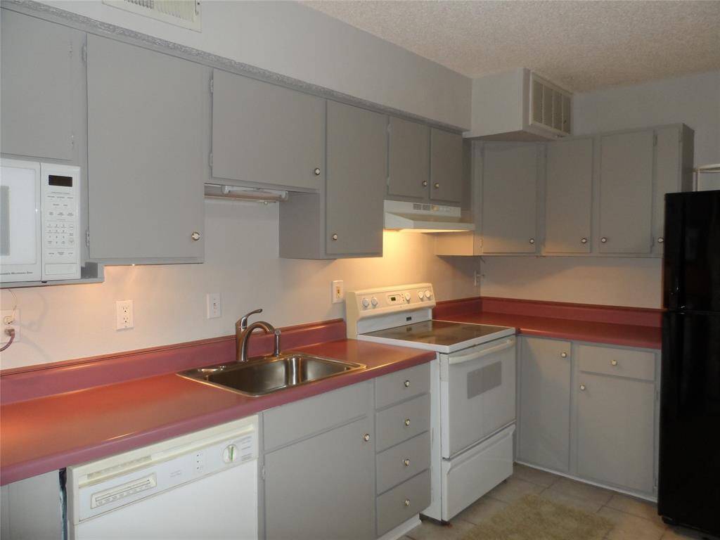 This kitchen features gray cabinetry with ample storage, and white appliances, including a stove, dishwasher, and microwave. It has a double sink and a black refrigerator, offering a functional and cozy cooking space.