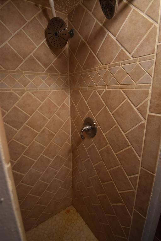 This photo shows a compact shower with beige, diagonal tile walls and dual showerheads, offering a functional and cozy bathing space.