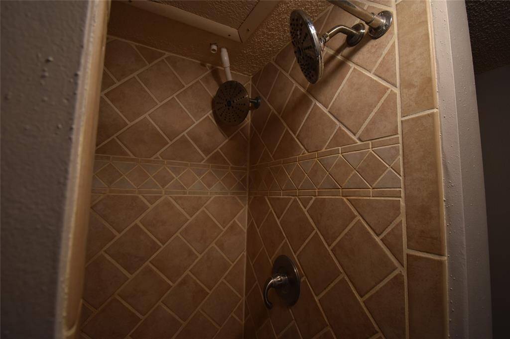 This photo shows a shower with dual shower heads and beige tile walls arranged in a diamond pattern, giving a modern and functional look to the bathroom.