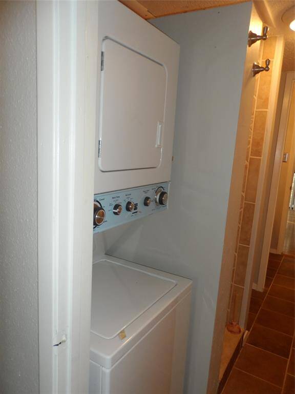 This photo shows a compact laundry area with a stacked washer and dryer unit, located in a primary bath with tiled flooring and neutral walls.