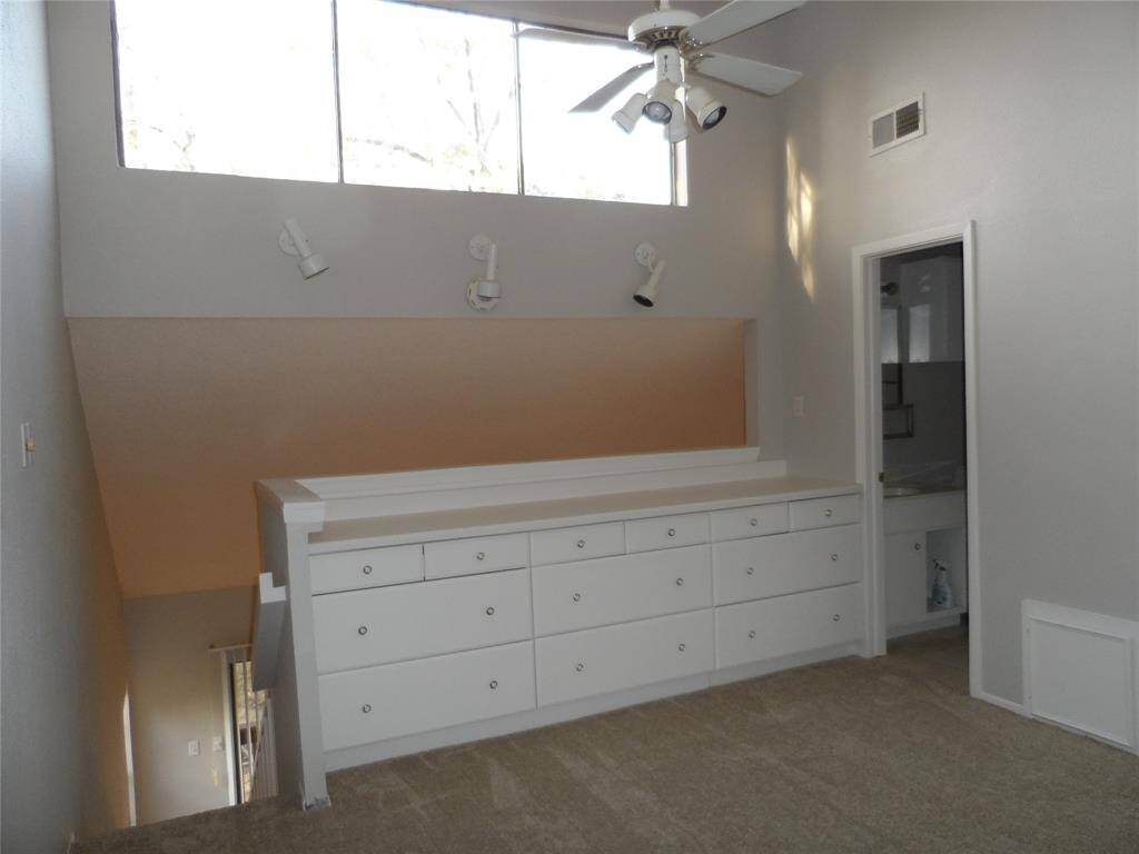 Bright, open loft area with a built-in dresser and overhead lighting. Features a ceiling fan and tall windows for natural light. Adjacent to the 2nd bathroom.
