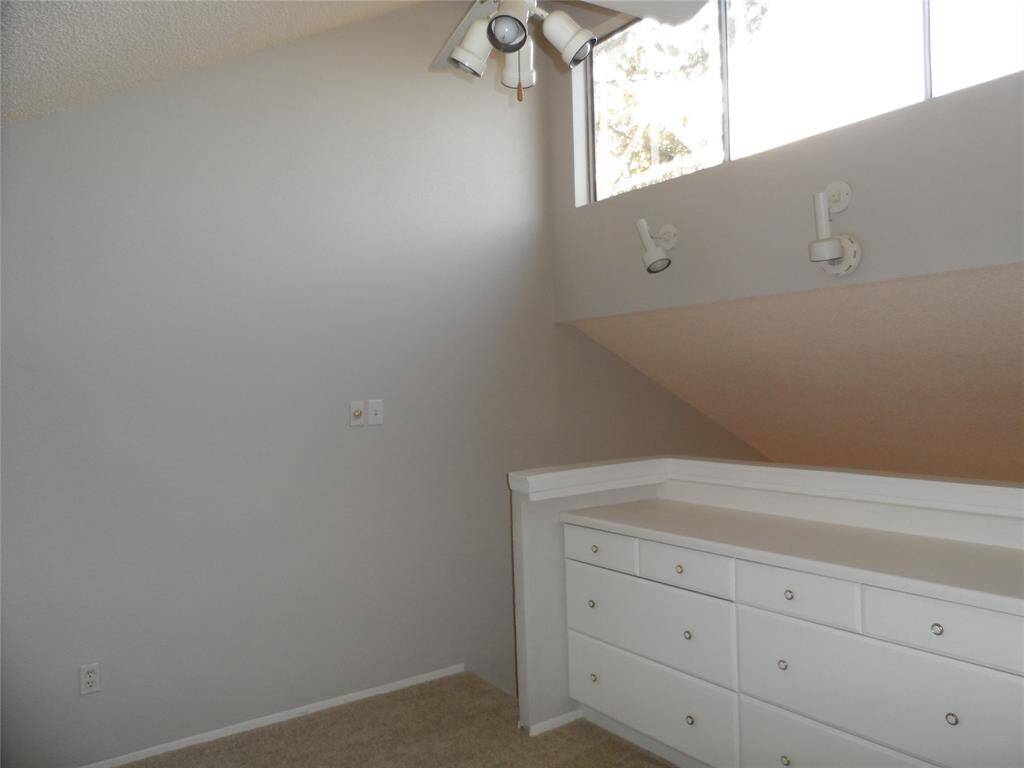angled ceiling and upper windows, featuring built-in white drawers and track lighting. The space has a neutral color scheme and carpeted flooring, ideal for a cozy nook or storage area.
