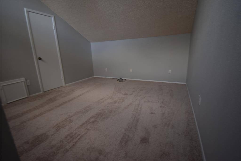 This room features a sloped ceiling and carpet, with soft gray walls, making it suitable for a bedroom or office.