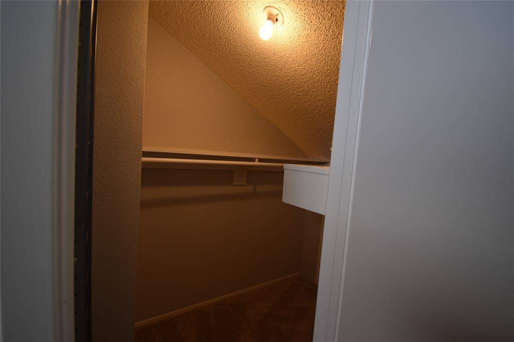 This photo shows a small, cozy closet with a sloped ceiling, and a rod for hanging clothes.