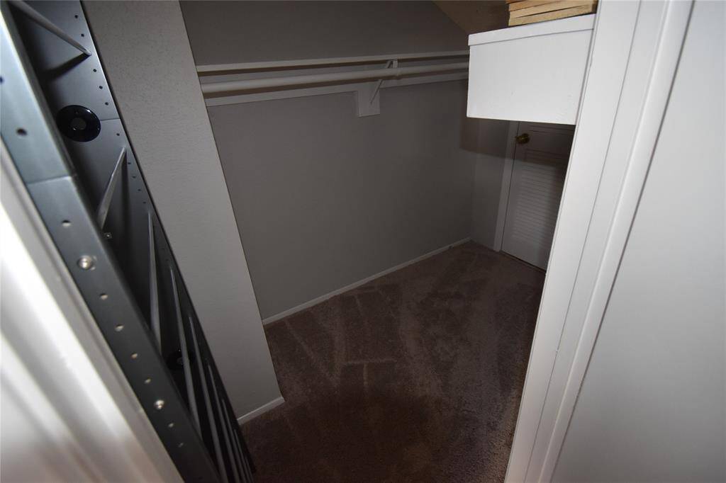 This photo shows a, carpeted walk-in closet with a clothes rod and shelf, suitable for additional storage or wardrobe space.