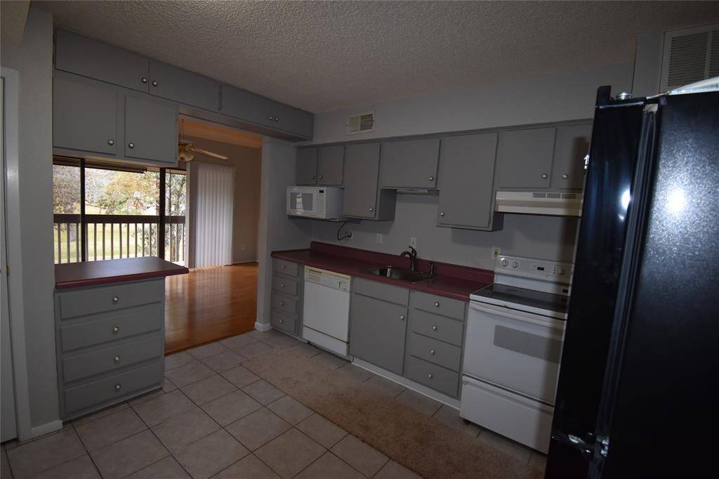 Cozy kitchen with gray cabinets, featuring a stove, dishwasher, and microwave. A large window offering natural light and a view of the outdoors.