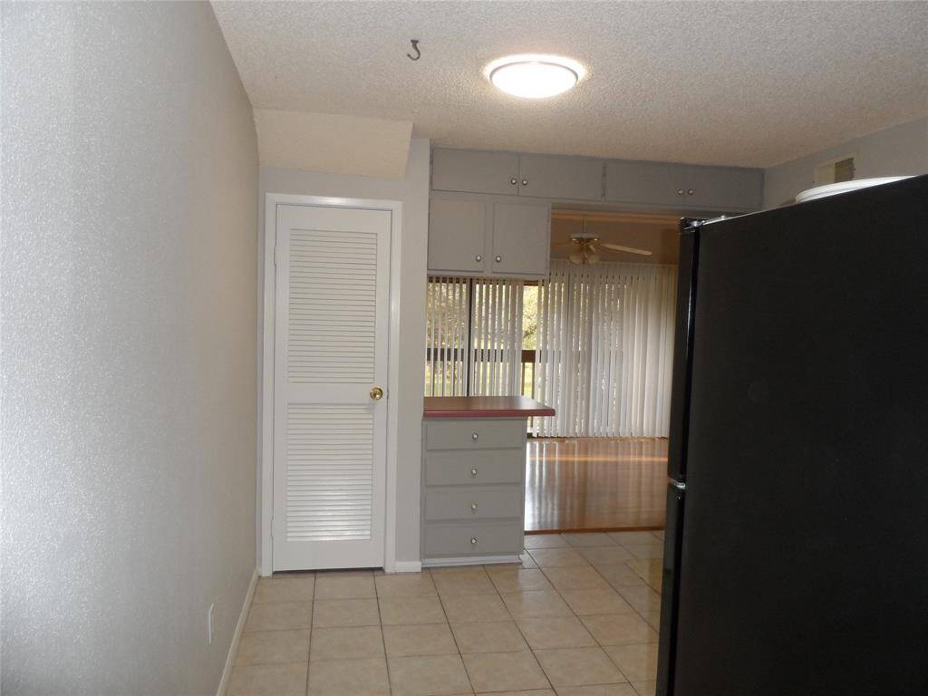 Walking into the kitchen with large windows and vertical blinds, providing natural light and a view of wood like floors.
