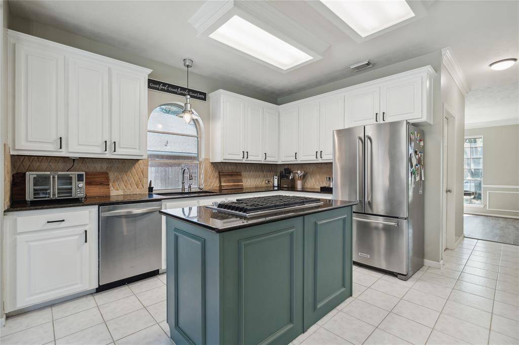 A closer look at the heart of the home reveals stunning detail—from the crown molding and tiled backsplash to the deep farmhouse sink framed by a charming arched window. The stainless steel appliances, double ovens, and generous counter space make meal prep easy, while the pop of green on the island adds character and warmth.