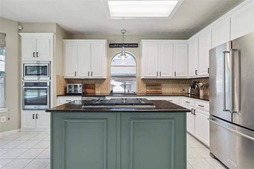 A symmetrical and stylish view showcases the full kitchen layout—complete with double ovens, stainless steel appliances, and a large arched window over the sink that brings in soft natural light