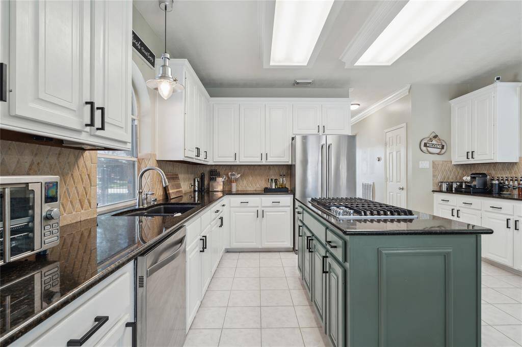 Get a closer look at the extensive counter space and sleek finishes. The wraparound granite countertops and decorative diamond-tile backsplash create a timeless look, while the pendant lighting adds a warm, modern touch
