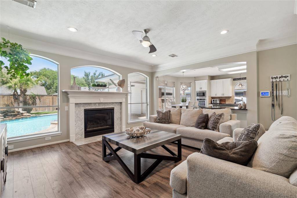 The centerpiece of the living room is a beautifully detailed fireplace framed by a chevron-patterned tile surround and flanked by large arched windows with pool views. Natural light pours in, giving the entire space a bright and airy feel.