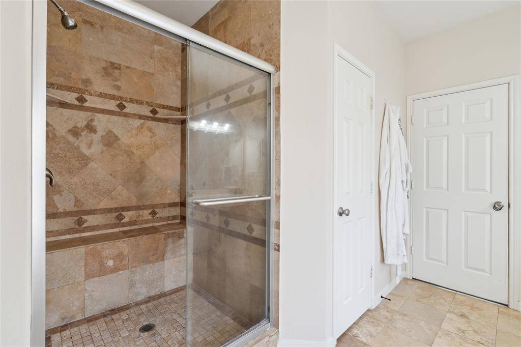 Unwind in this spacious walk-in shower, complete with warm-toned natural stone tile, built-in bench seating, and a sleek glass enclosure.