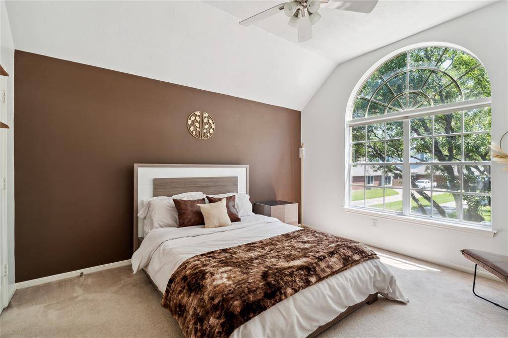 This charming upstairs bedroom is filled with light thanks to a dramatic arched window. Vaulted ceilings give it an airy feel, while plush carpeting and neutral tones make it cozy for any age.