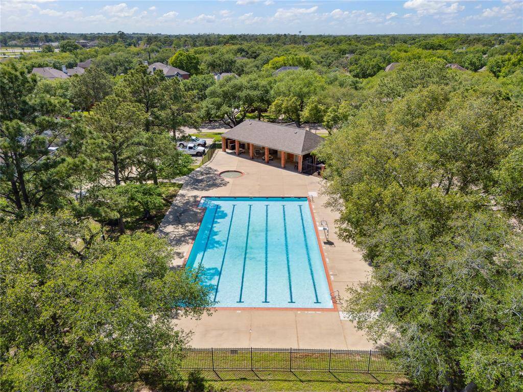 An overhead view showcases the expansive Olympic-style pool nestled under a canopy of mature trees, providing a serene escape within the neighborhood. The pool house with covered seating, a smaller kiddie pool, and open concrete deck make this a central hub for relaxation and community gatherings.