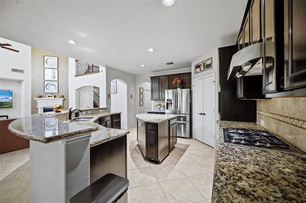 Modern kitchen with dark wood cabinetry, granite countertops, and a central island, elegant tile flooring.