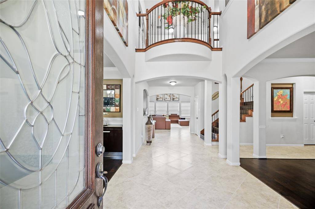This entryway features a grand, open design with high ceilings and elegant arches. A beautifully detailed glass front door opens into a space with tile flooring, leading to a living area with a staircase