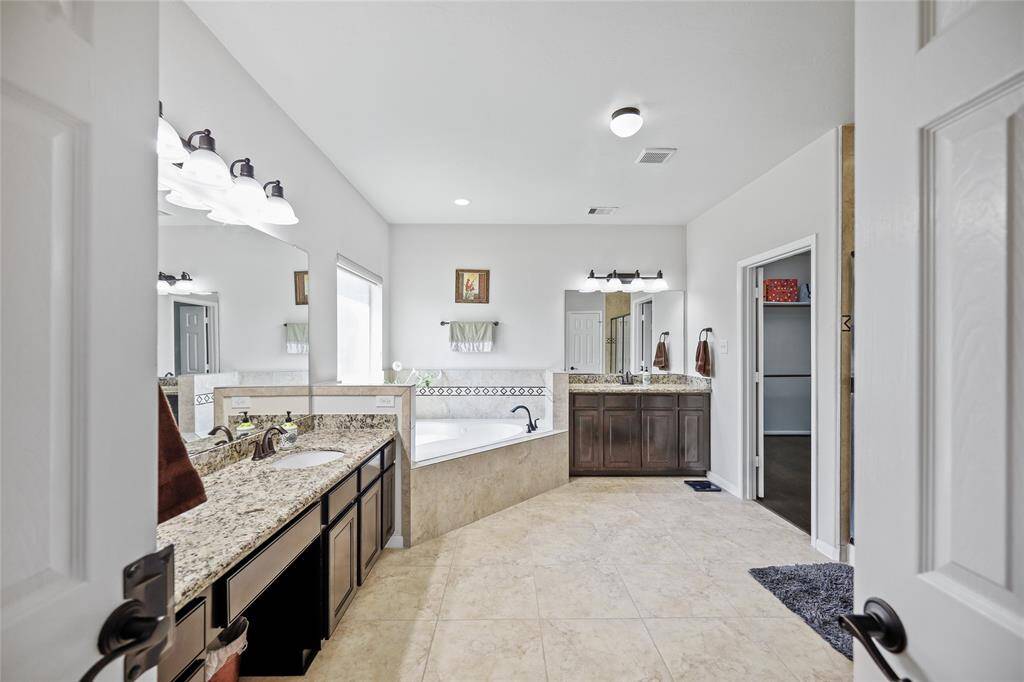 This spacious primary bathroom features elegant granite countertops and neutral tile flooring add to clean, sophisticated look.