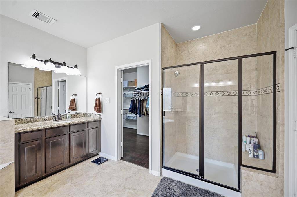 The primary en-suite features a spacious walk-in shower with glass doors, a double vanity with granite countertops, and dark wood cabinetry.