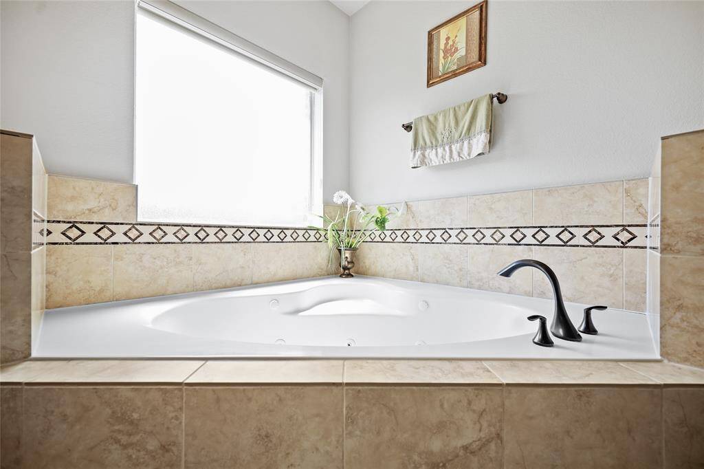 Luxurious bathroom featuring a large, corner jetted tub with elegant tile surround and modern fixtures. Natural light streams in through a frosted window, enhancing the serene atmosphere.