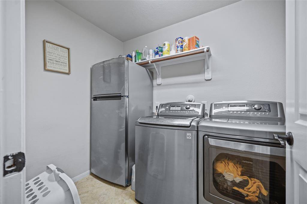 Expansive utility room accommodating washer, dryer, and additional fridge with ample storage space.