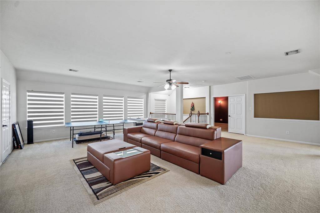 This inviting game room boasts large windows for ample natural light, a ceiling fan, and neutral carpeting, perfect for relaxation or entertainment.