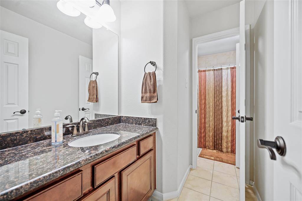 This bathroom features a granite countertop with triple sinks, wood cabinetry, and neutral wall colors.