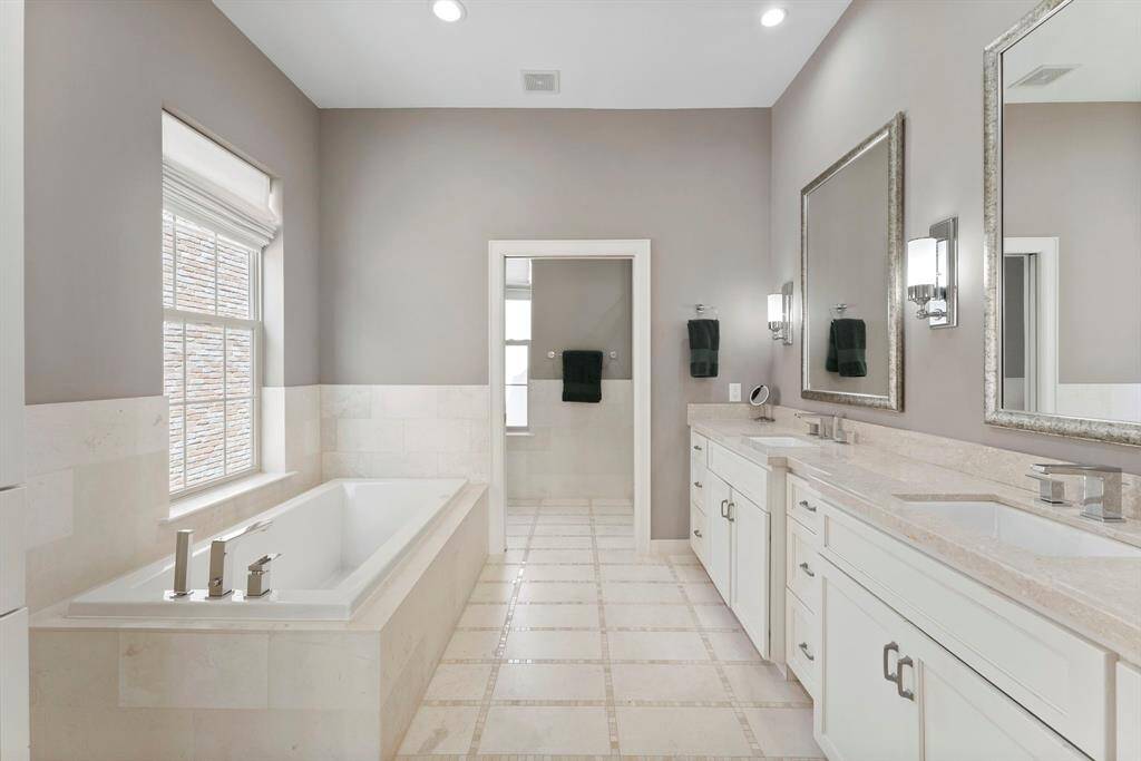 Spa-inspired primary bathroom with tile flooring, dual sinks, jetted tub, and an oversized walk-in shower.