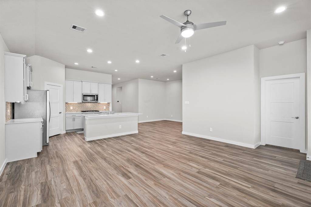 This view captures the full openness of the main living area as it flows effortlessly into the kitchen. The strategic placement of windows, recessed ceiling lights, and clean lines reinforce the home’s modern architectural integrity and layout efficiency.