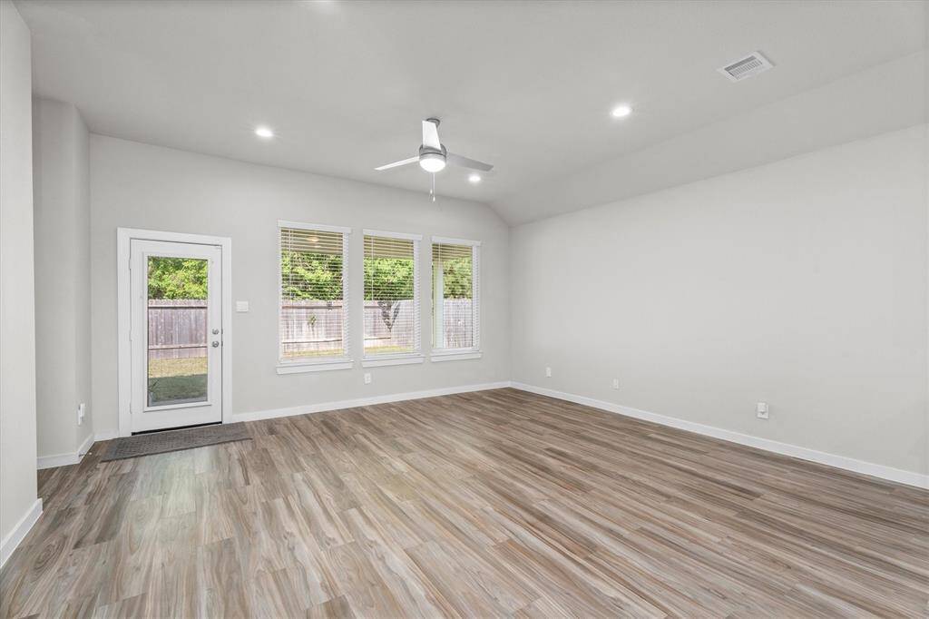 Bright and airy, the living room features a trio of tall windows overlooking the backyard, providing ample natural light. A ceiling fan adds comfort and functionality, while the back door offers easy access to the covered patio and yard beyond.