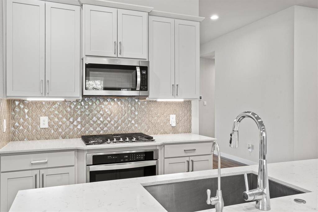 The gourmet kitchen features white shaker-style cabinetry with modern brushed nickel hardware. A sleek stainless steel Whirlpool appliance suite—including a built-in microwave, gas cooktop, and oven—is paired with an eye-catching mosaic tile backsplash in a shimmering geometric pattern, adding texture and elegance to the workspace.