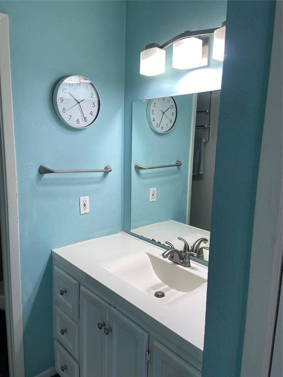 This bathroom features a clean, modern design with light blue walls, a white vanity with ample storage, and a large mirror. It includes a sleek faucet, and contemporary lighting