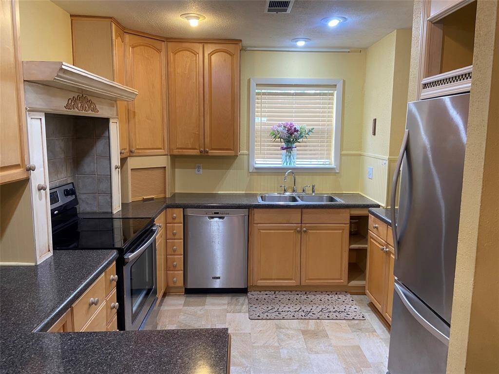 This spacious kitchen features warm wood cabinetry, granite countertops, and modern stainless steel appliances. The  double sink beneath the window creates a bright and inviting cooking space.