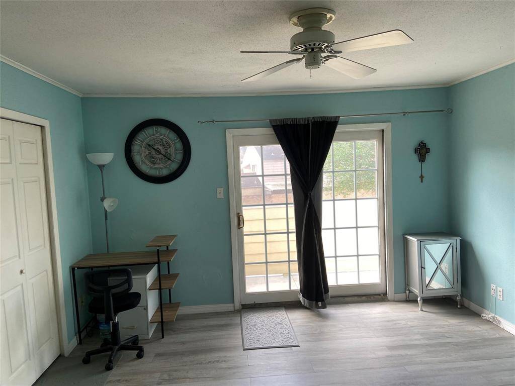 This primary bedroom room features a bright, airy space with light blue walls and natural light from glass doors leading outside to the balcony.