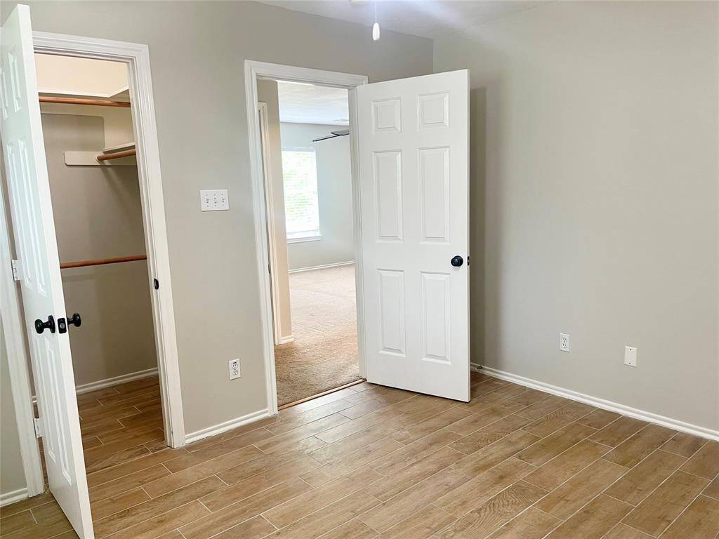 This photo shows a hallway with light wood flooring and neutral walls. A partially open door reveals a half bathroom with a pedestal sink and tile floor. The area has a clean and modern look, with a staircase leading upwards.
