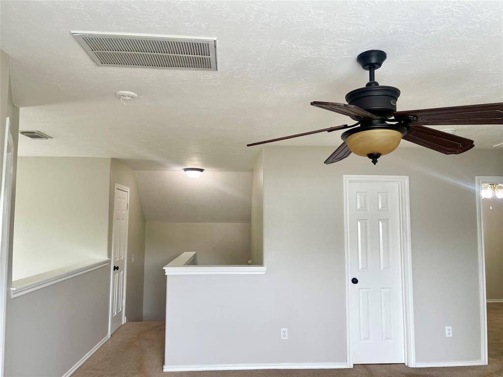 This Game room features neutral-toned walls and carpet, a ceiling fan with light, and multiple doors leading to adjacent areas. It has a clean, open layout with a partial wall and railing, creating a spacious feel.