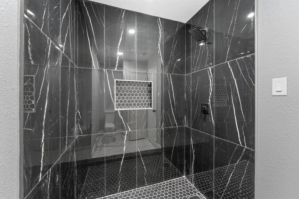 Modern elegance shines in this primary bath with marble-inspired tile, double vanity, and striking black accent throughout.
