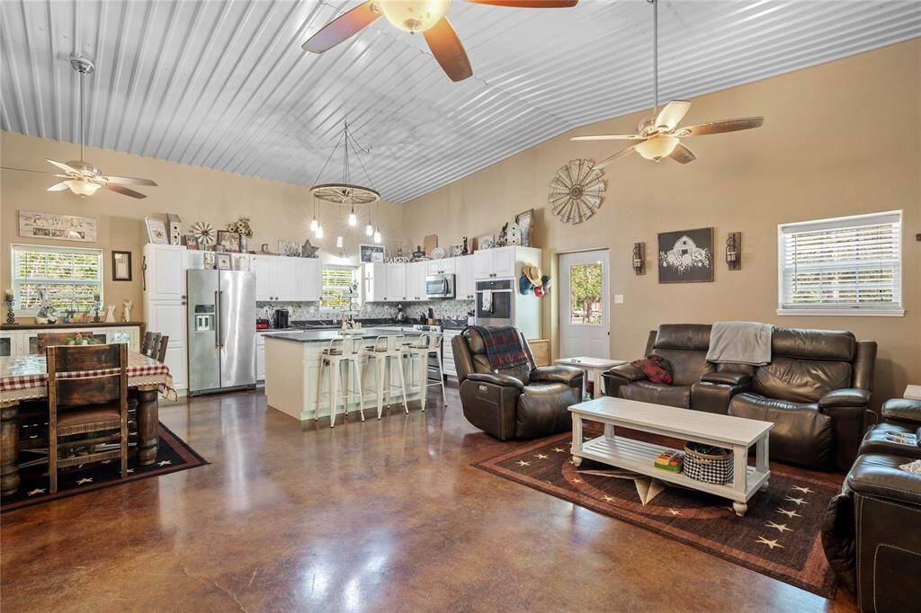 Step inside to an inviting open concept living area that perfectly blends modern convenience with cozy country charm. Vaulted ceilings with exposed corrugated metal add a touch of industrial flair, while the warm stained concrete floors provide durability and rustic elegance throughout. Whether you're hosting a crowd or enjoying a quiet night in, this open-plan design offers flexibility, warmth, and the perfect place to call home.