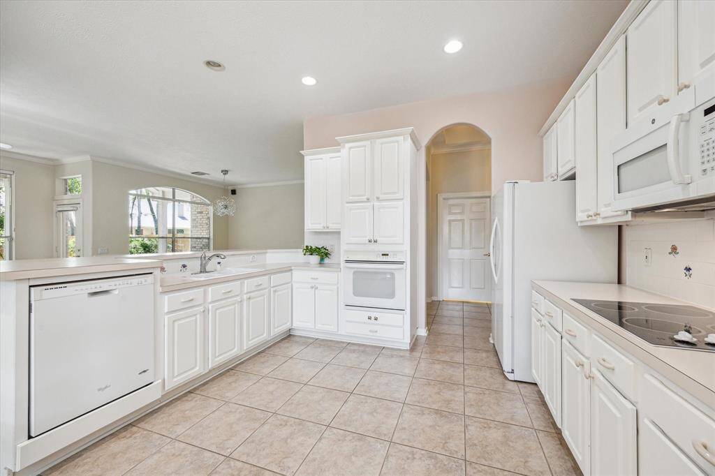 This expansive kitchen boasts an abundance of cabinetry, offering plenty of storage while maintaining a open, light-filled ambiance. High ceilings further enhance the bright and airy atmosphere, while large windows provide stunning views of the generous backyard oasis.
