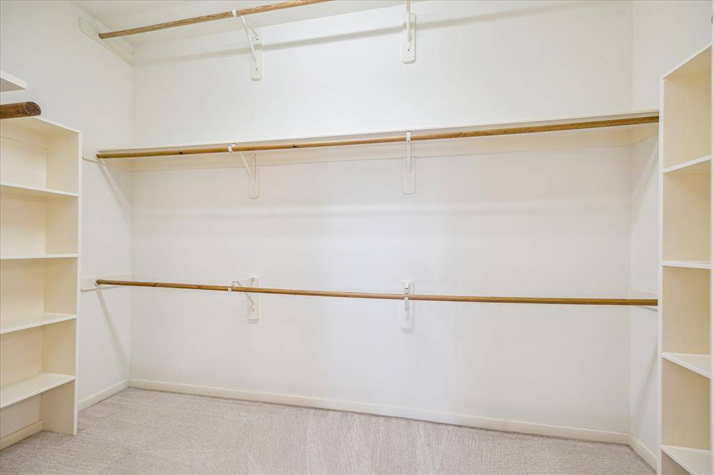 The large primary walk-in closet features three rows of hanging space, providing ample room for organization. High ceilings add to the open feel, while shelving on both sides offers additional storage options for a well-organized space.