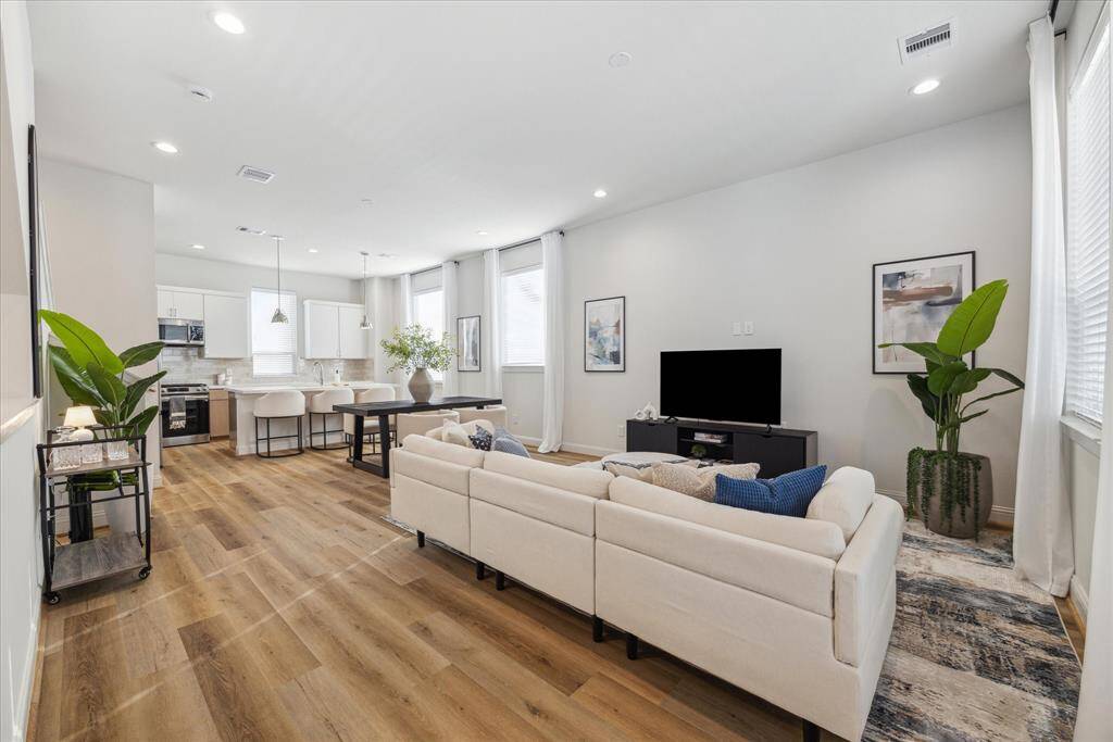 This spacious open-concept living area seamlessly flows into a modern kitchen, offering a perfect layout for both relaxation and entertainment. The light-colored flooring enhances the bright and airy feel, while large windows allow for plenty of natural light. The kitchen features sleek cabinetry, a large quartz island, and stainless steel appliances, creating a functional and stylish space ideal for both everyday living and hosting guests.