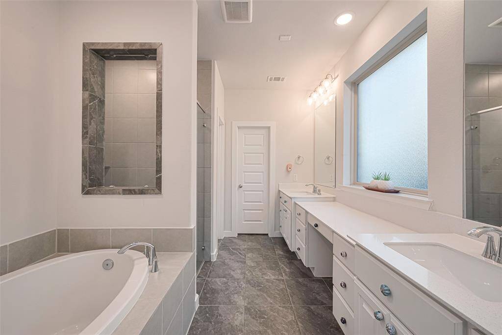 A spa-like primary ensuite featuring double vanities, a center picture window, walk-in shower, soaking tub, and an abundance of counter and storage space.