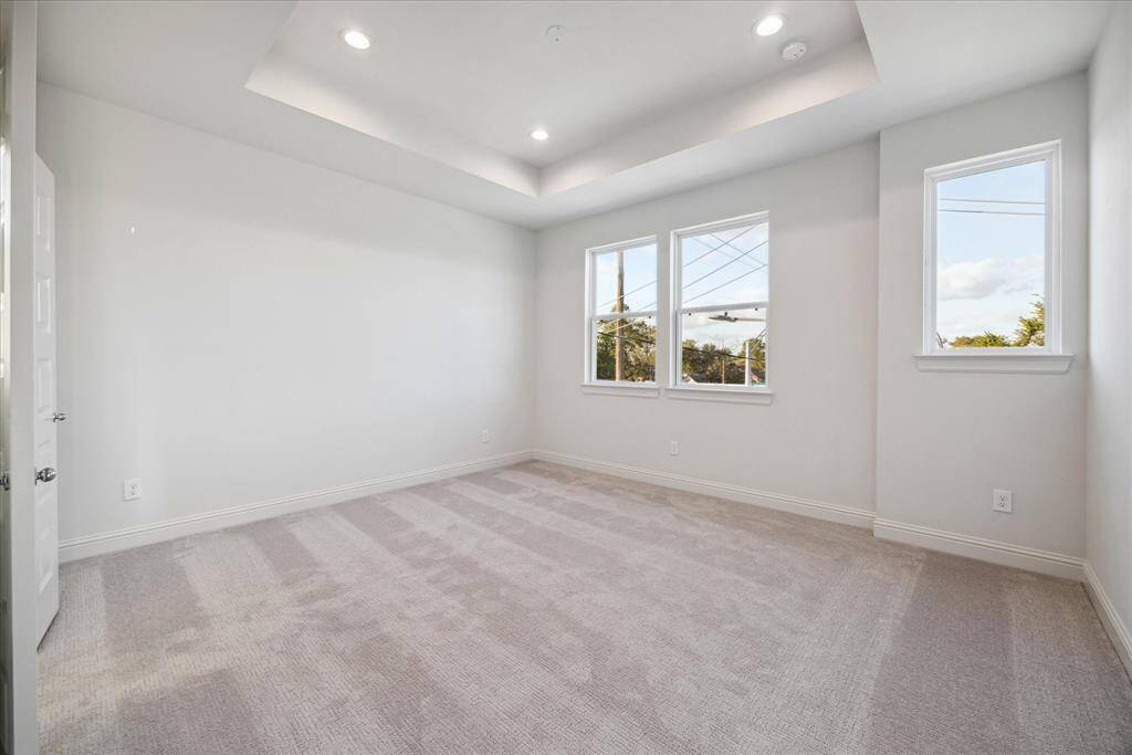 Located on the third floor, this serene primary bedroom offers a peaceful retreat with its soft neutral palette, plush carpeting, and tray ceiling detail. Large windows flood the space with natural light, creating a bright and airy ambiance. With plenty of space for furniture and design personalization, this room provides a perfect sanctuary at the end of the day.