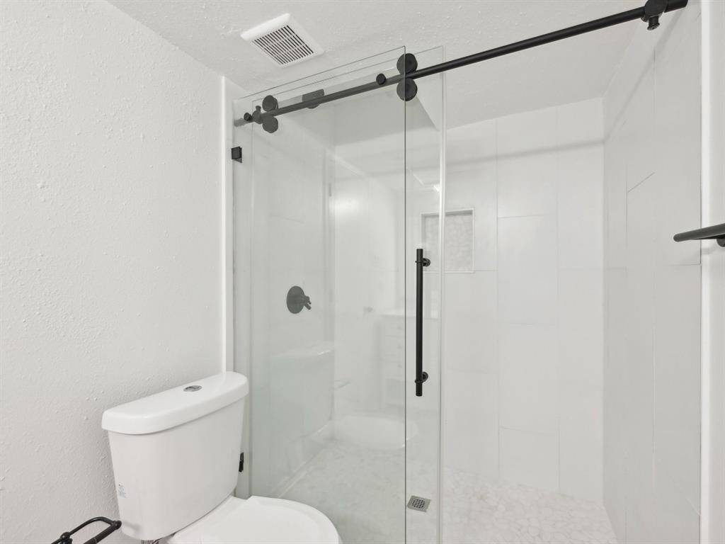 The beautifully updated shower has a sliding, frameless door. Notice the dual flush toilet, too!