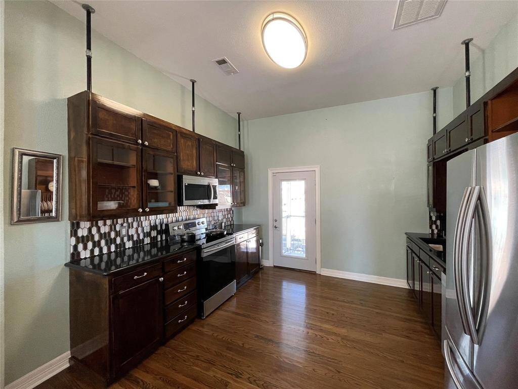 This chef kitchen features modern stainless steel appliances, dark wood cabinetry, and a unique tiled backsplash.
