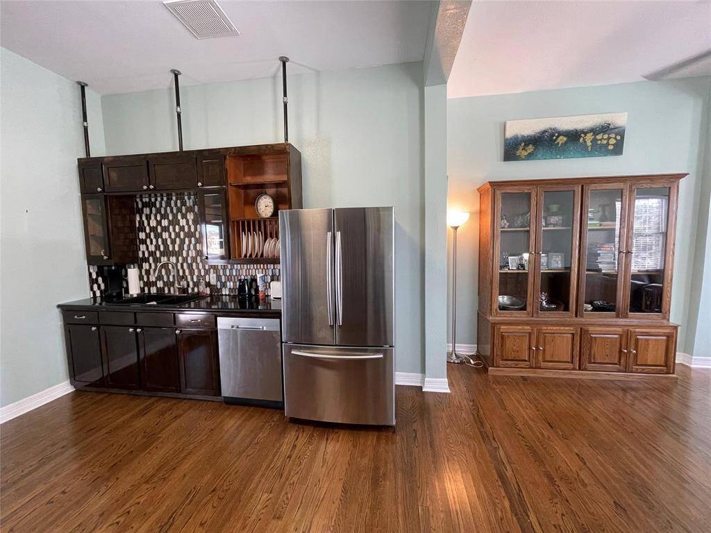 This room features a modern kitchen with new cabinetry, a stainless steel refrigerator, and a stylish tile backsplash. The hardwood floors add warmth.